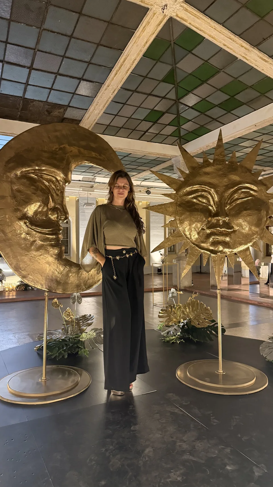 Rezi standing between a golden moon and a golden sun sculpture at an event