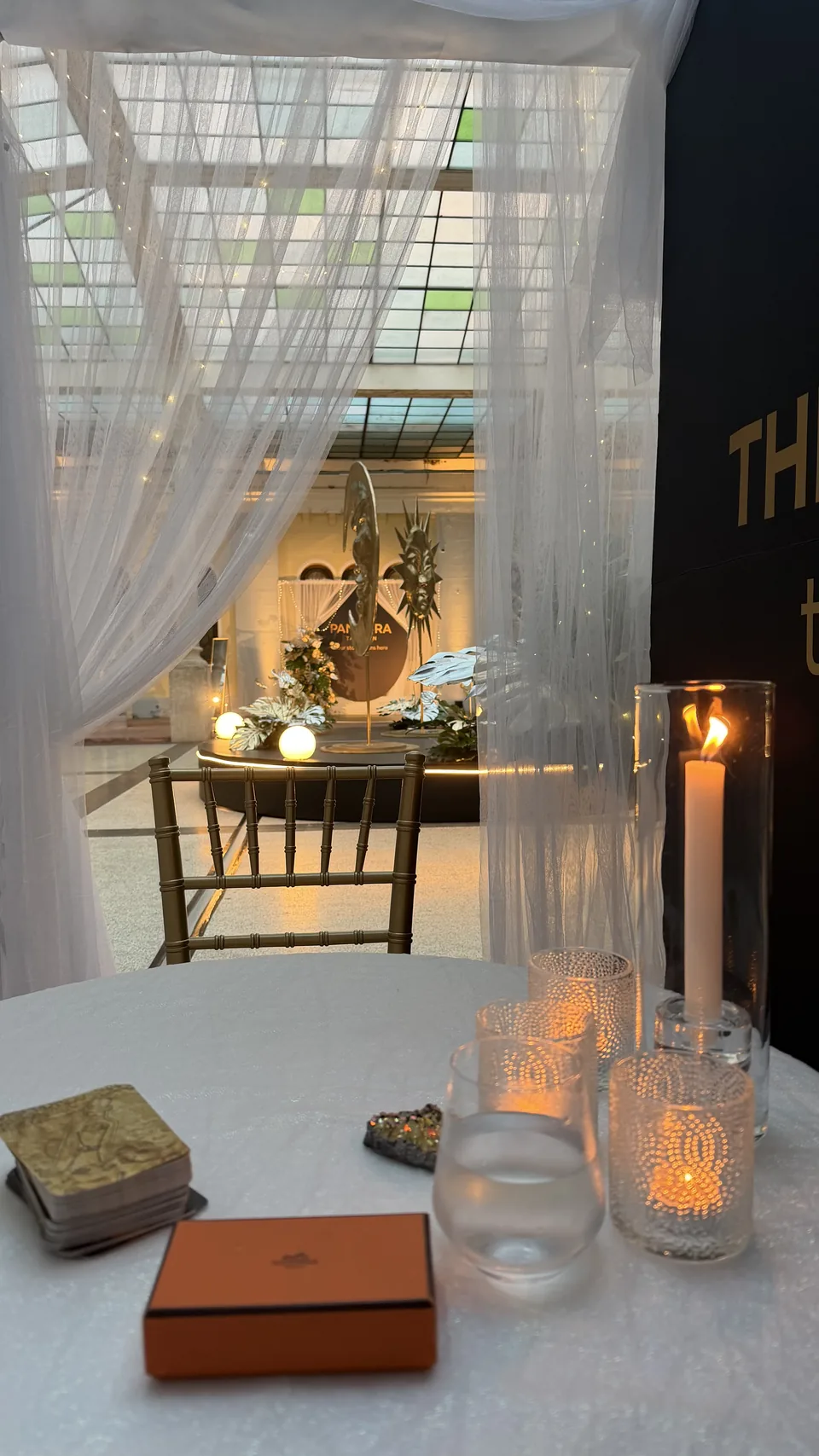A white-clothed reading table with a deck of cards, candles and sheer curtains at an event
