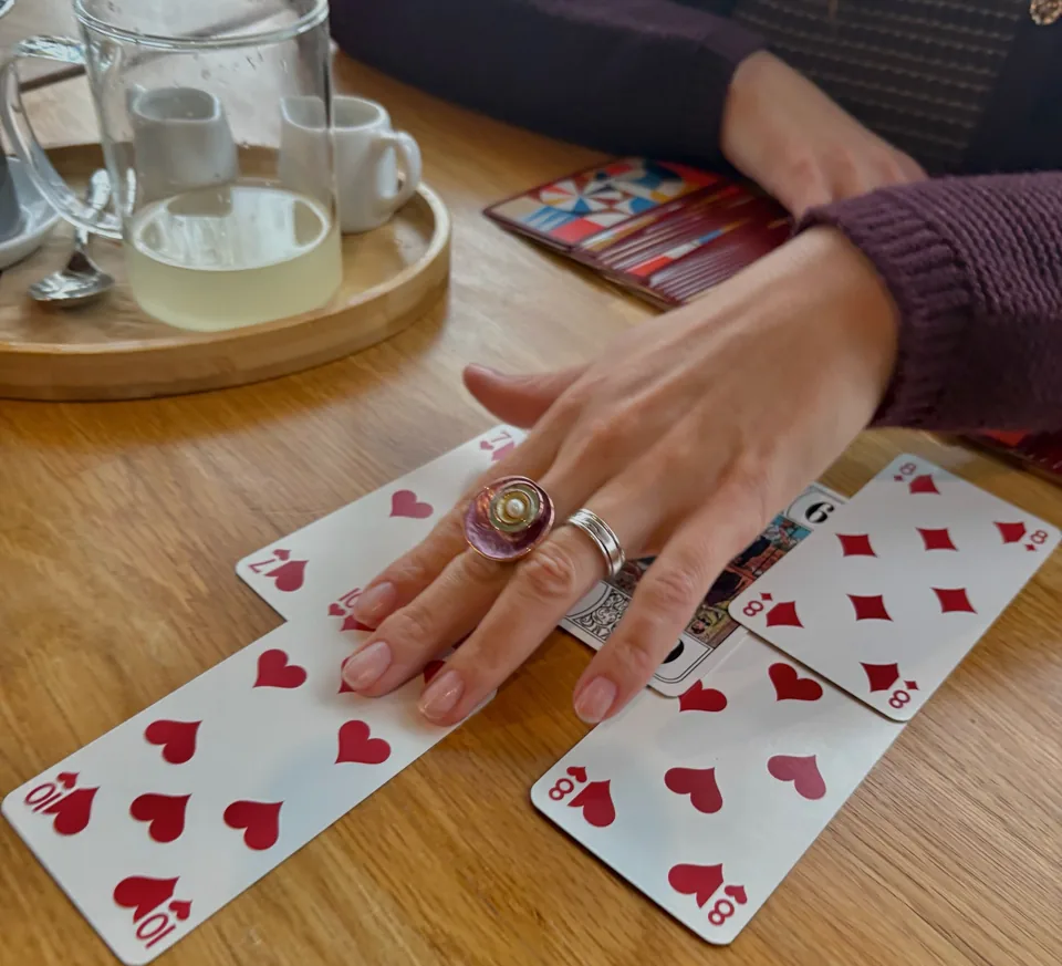 Rezi’s hand over a spread of playing cards with hearts and clubs